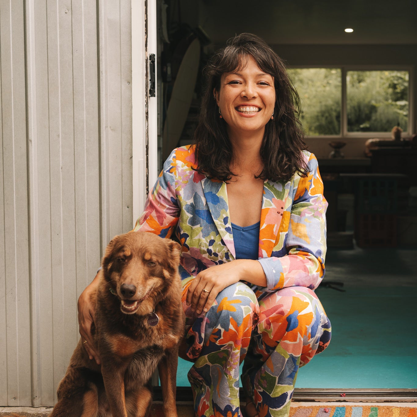 Woman in colorful outfit sitting with a dog in front of a studio entrance