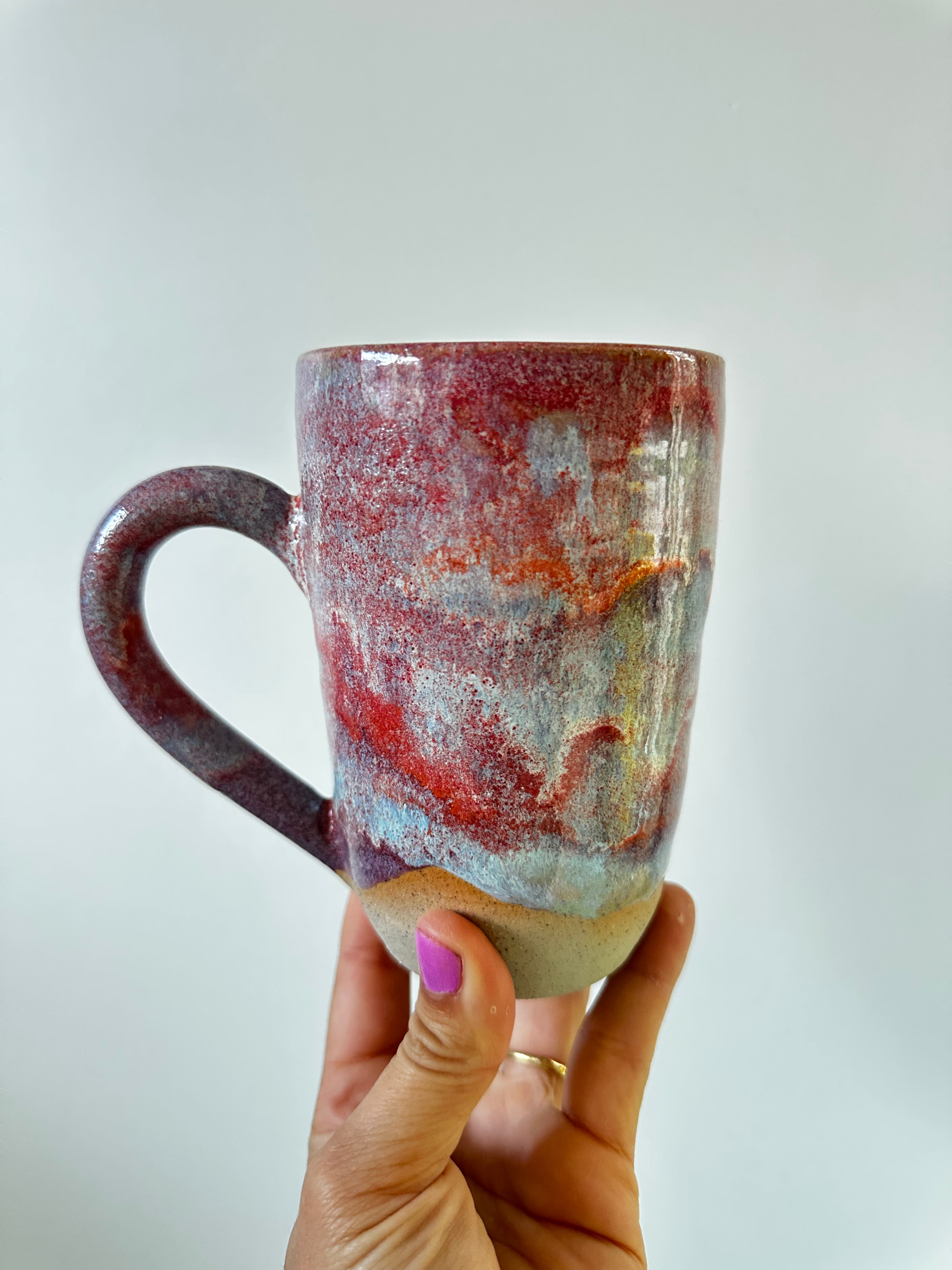A hand holds up a very large colourful mug
