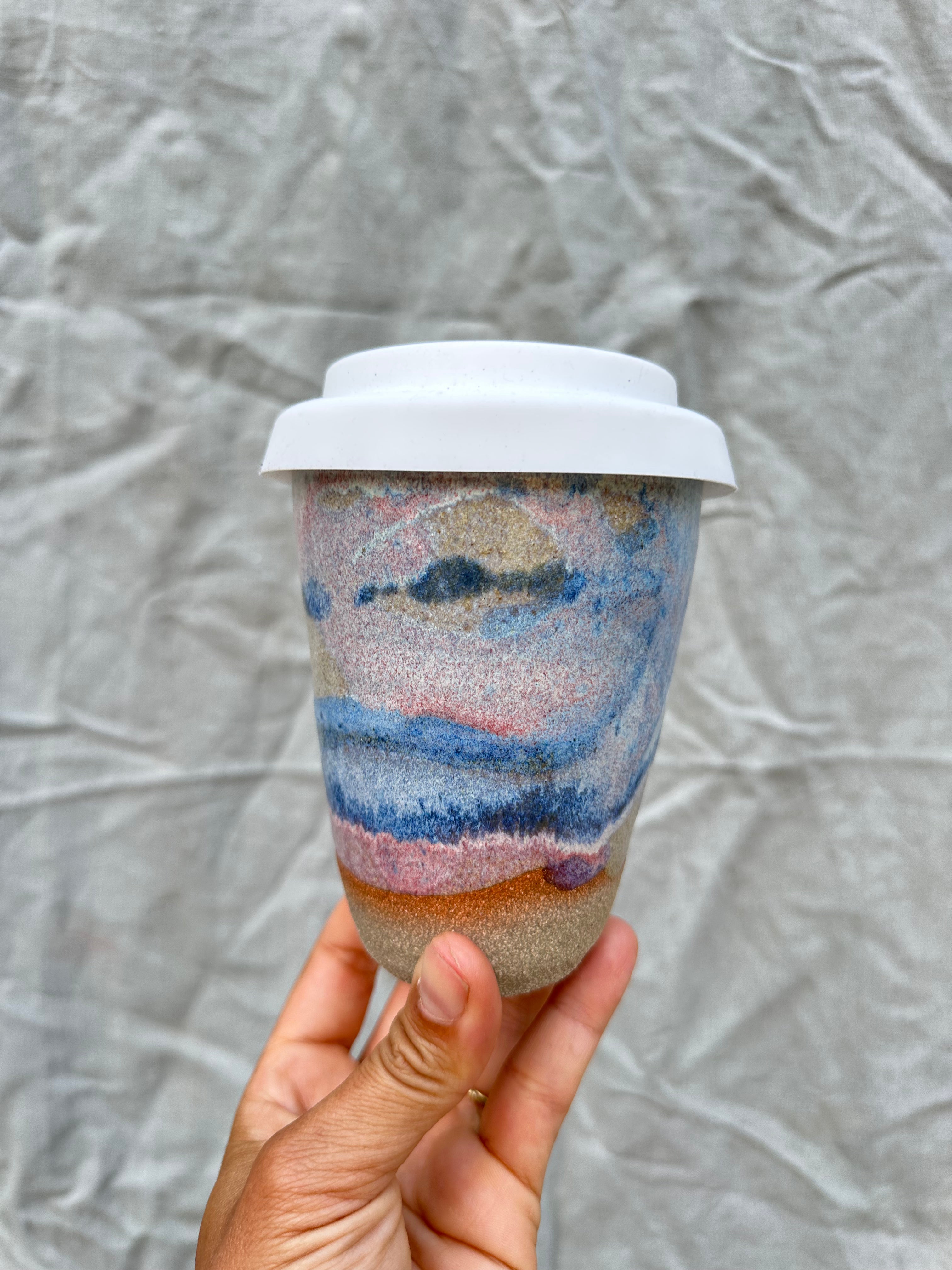 handmade cup with white silicone lid against a grey background