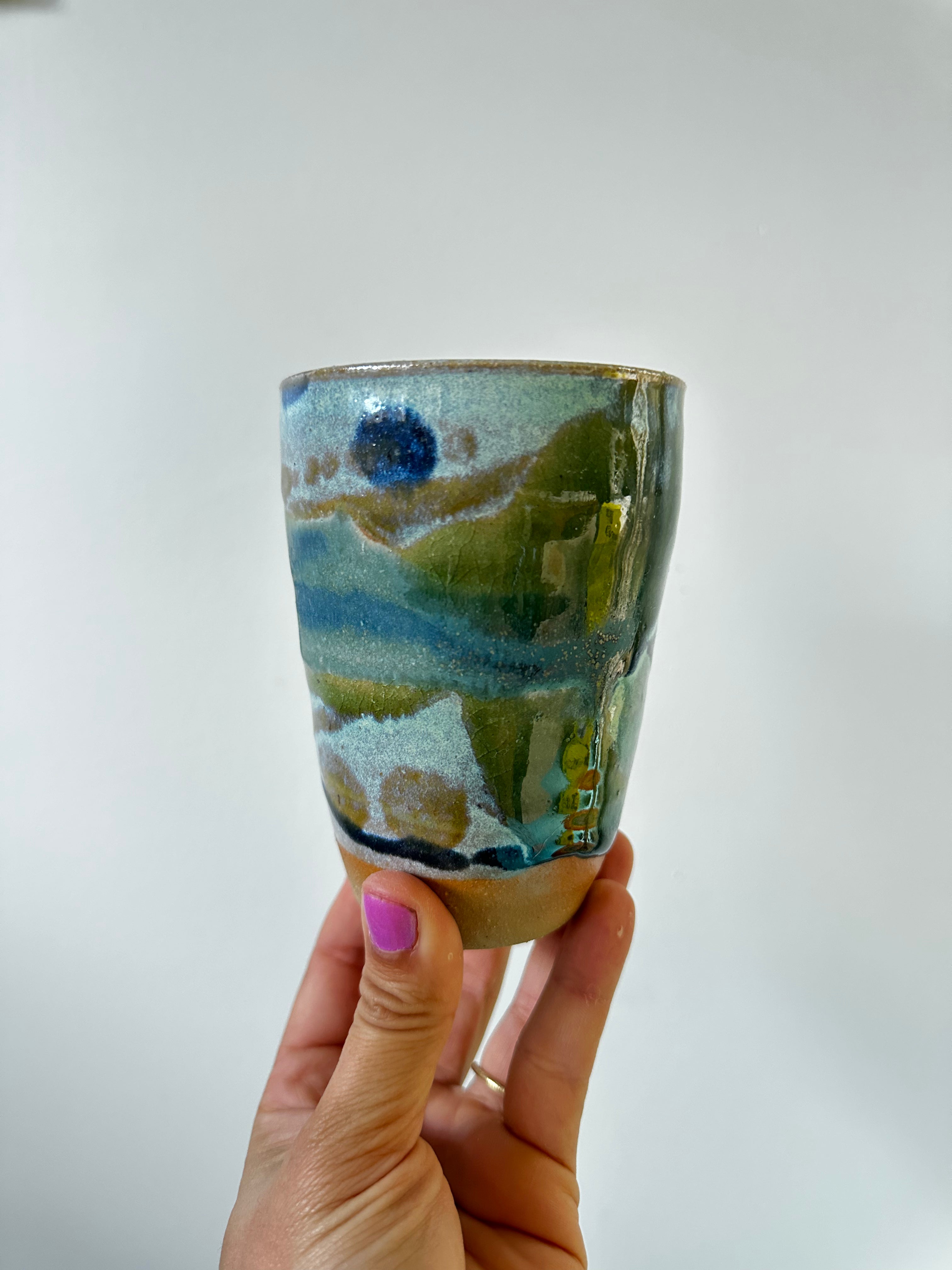 A hand holds up a green and blue cup