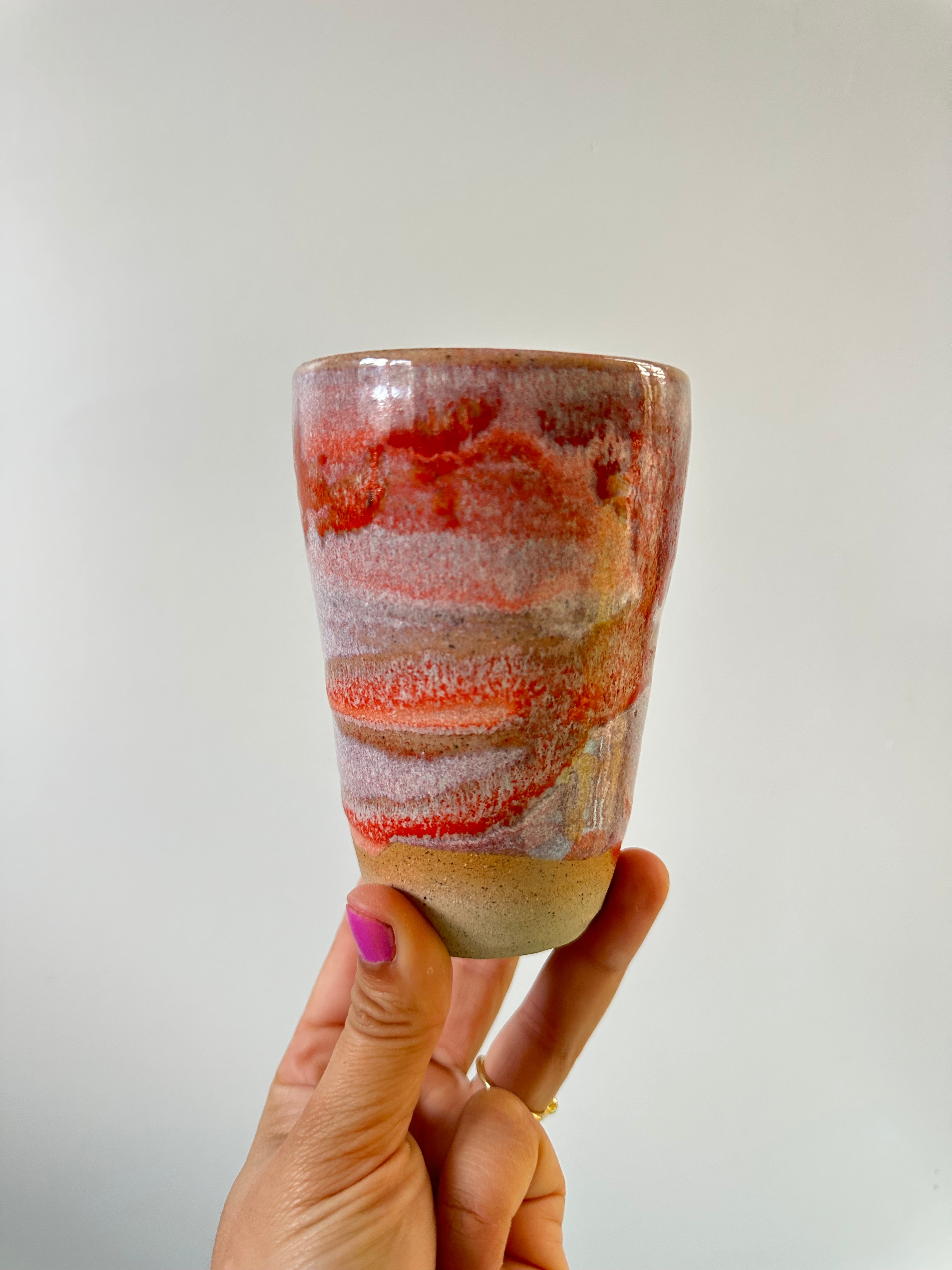 A hand holds up a cup with orange and pink