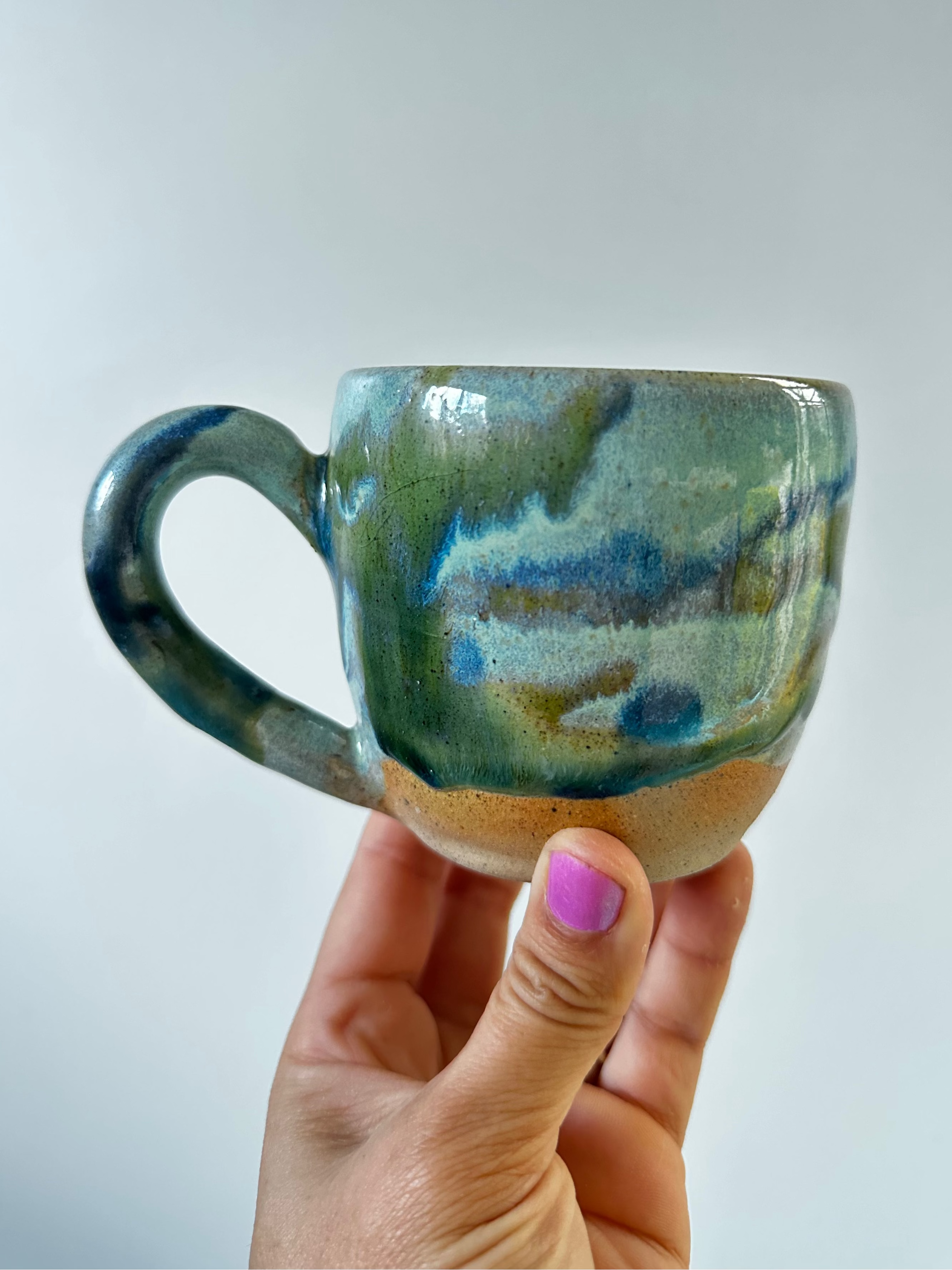A hand holds up a mug in landscape greens and blues