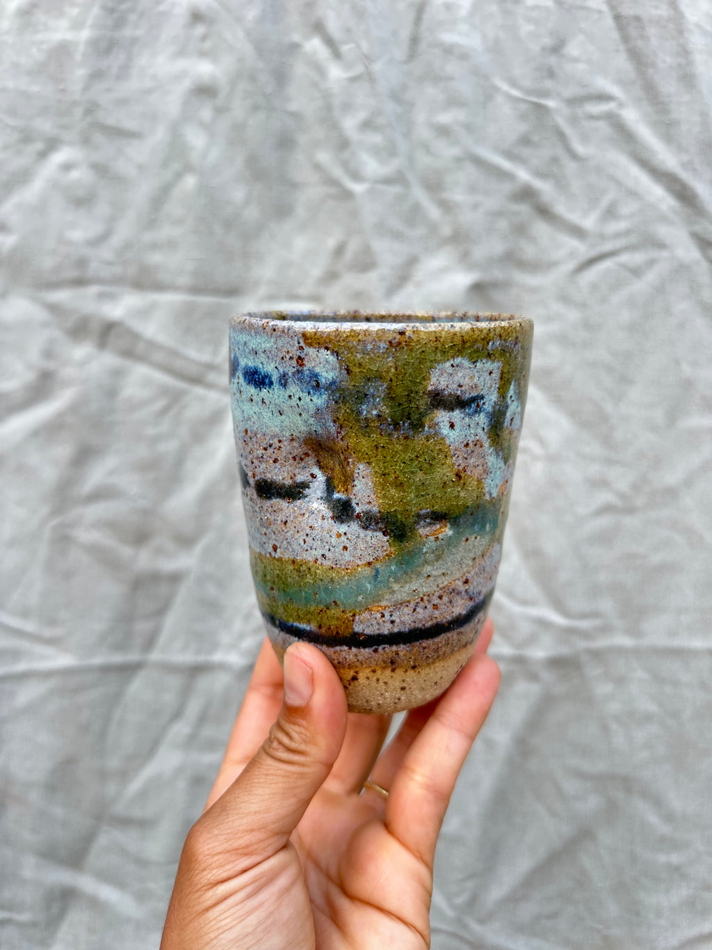 hand holds up a cup inspired by scenery on a grey background