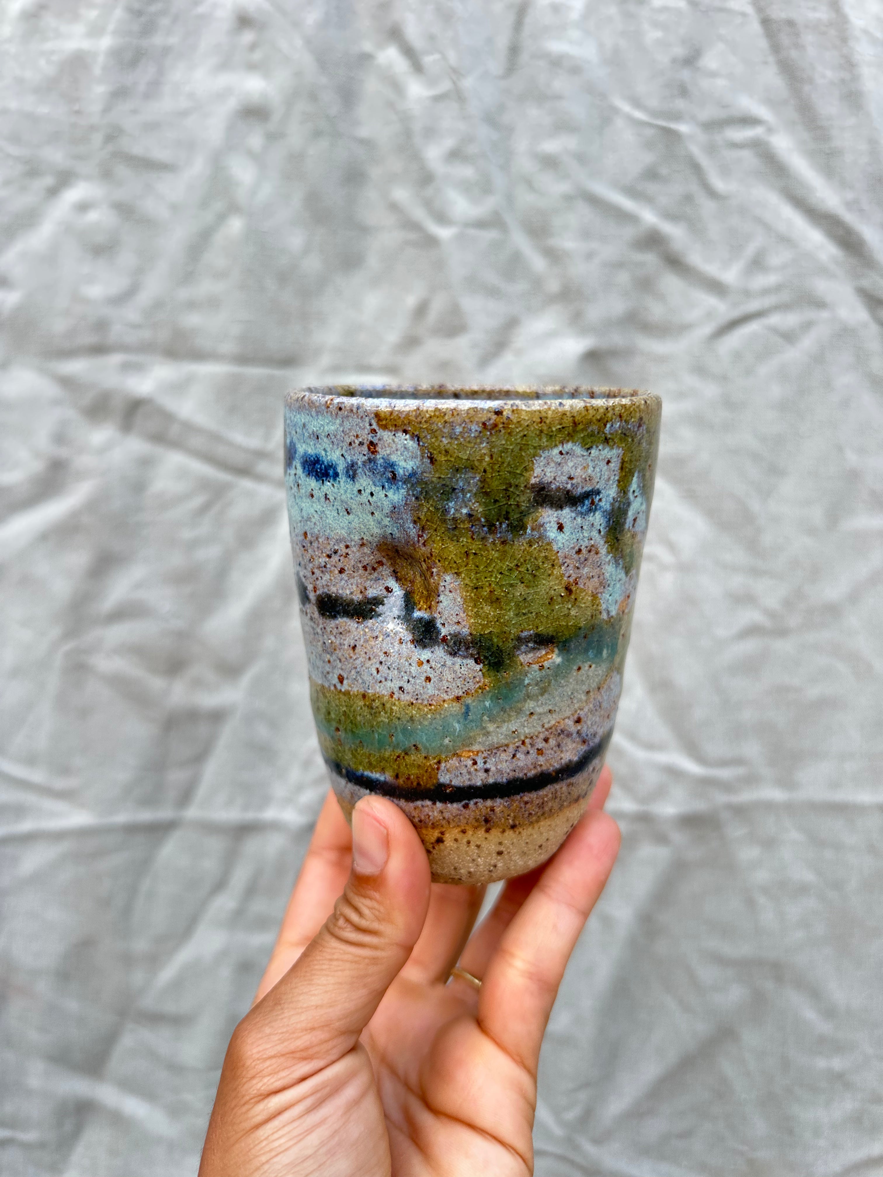 hand holds up a cup inspired by scenery on a grey background