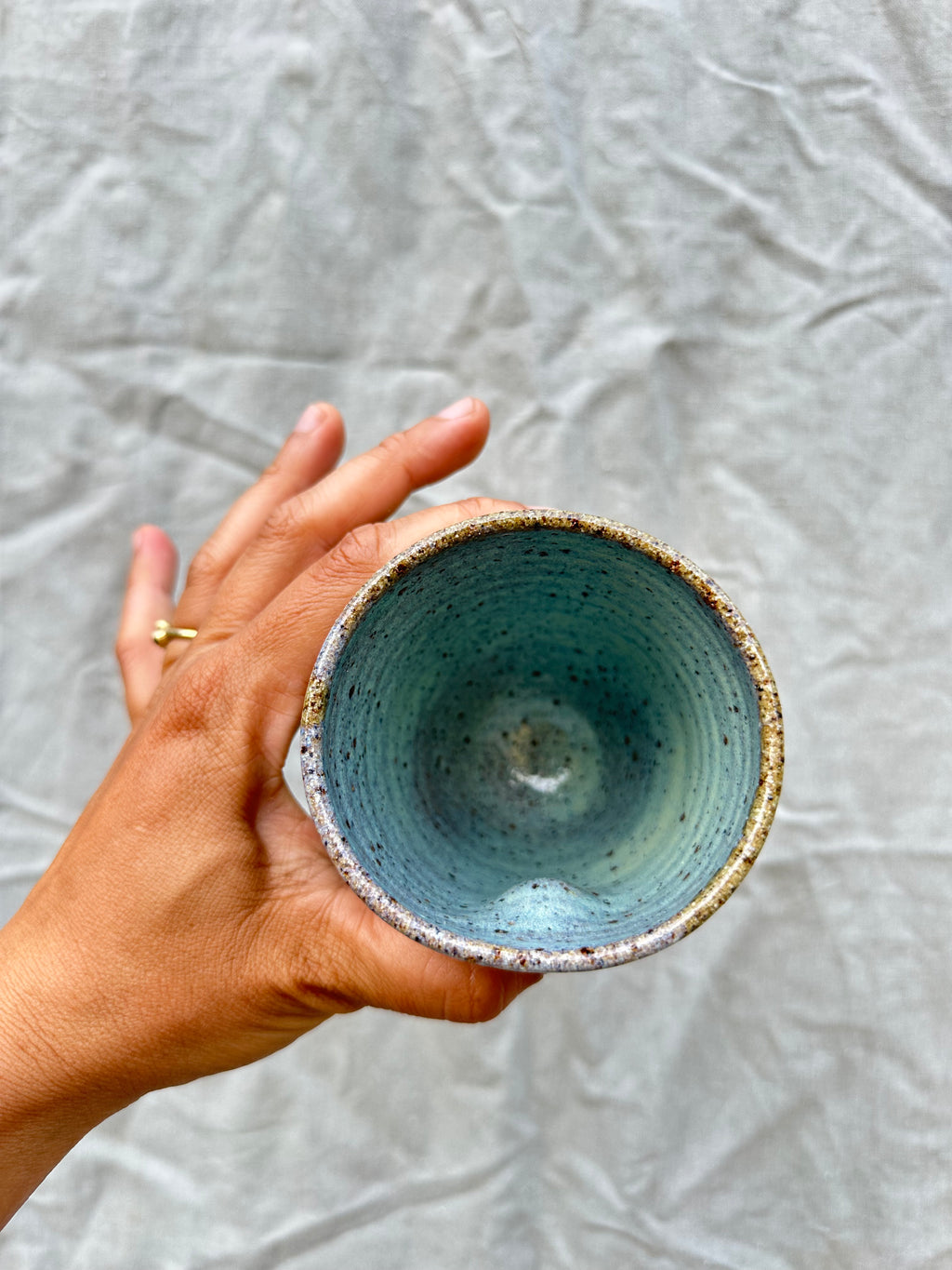 Hand holding a ceramic cup so you can see inside with a textured surface against a gray background