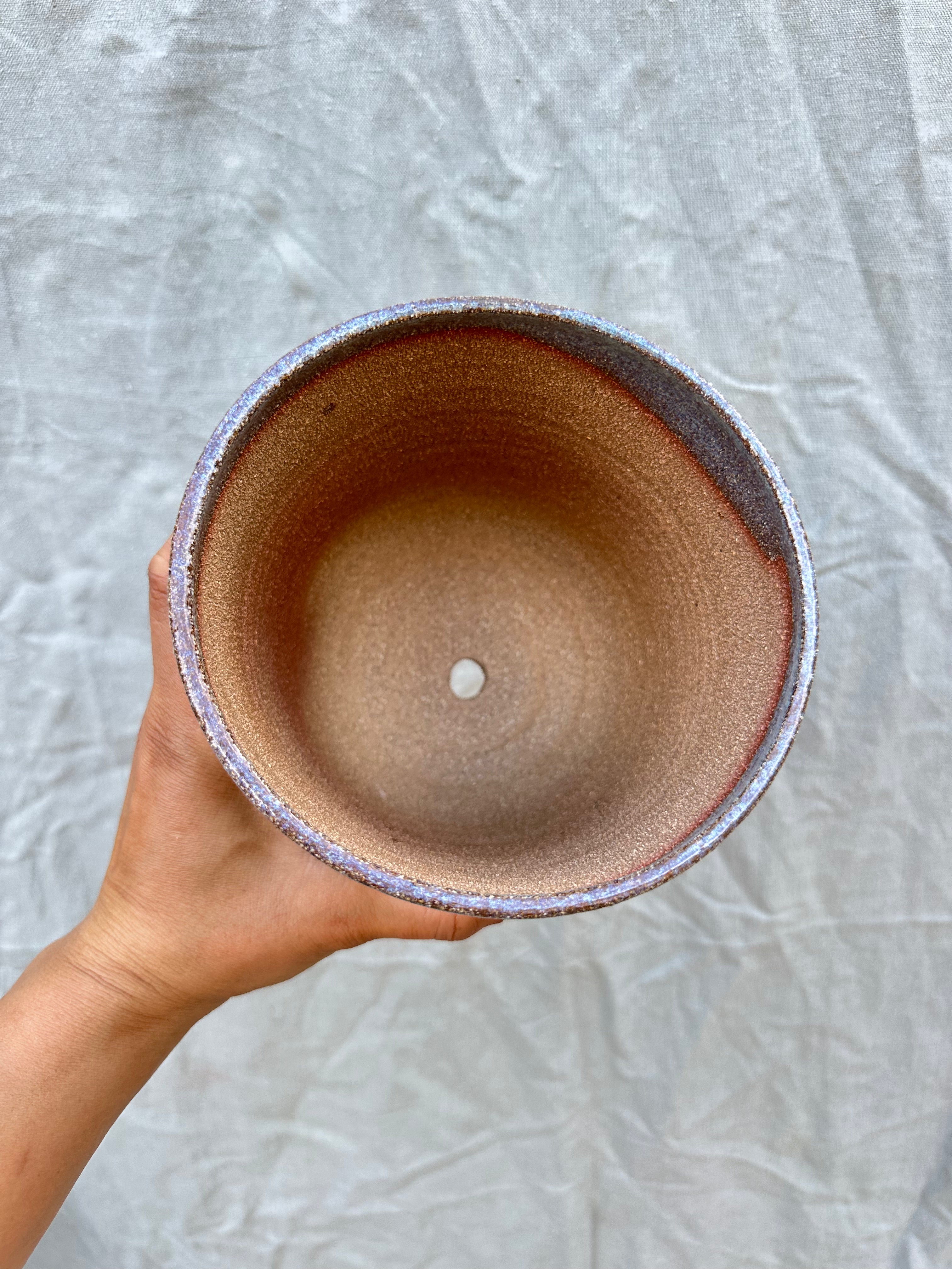 Hand holding a ceramic planter against a textured gray background