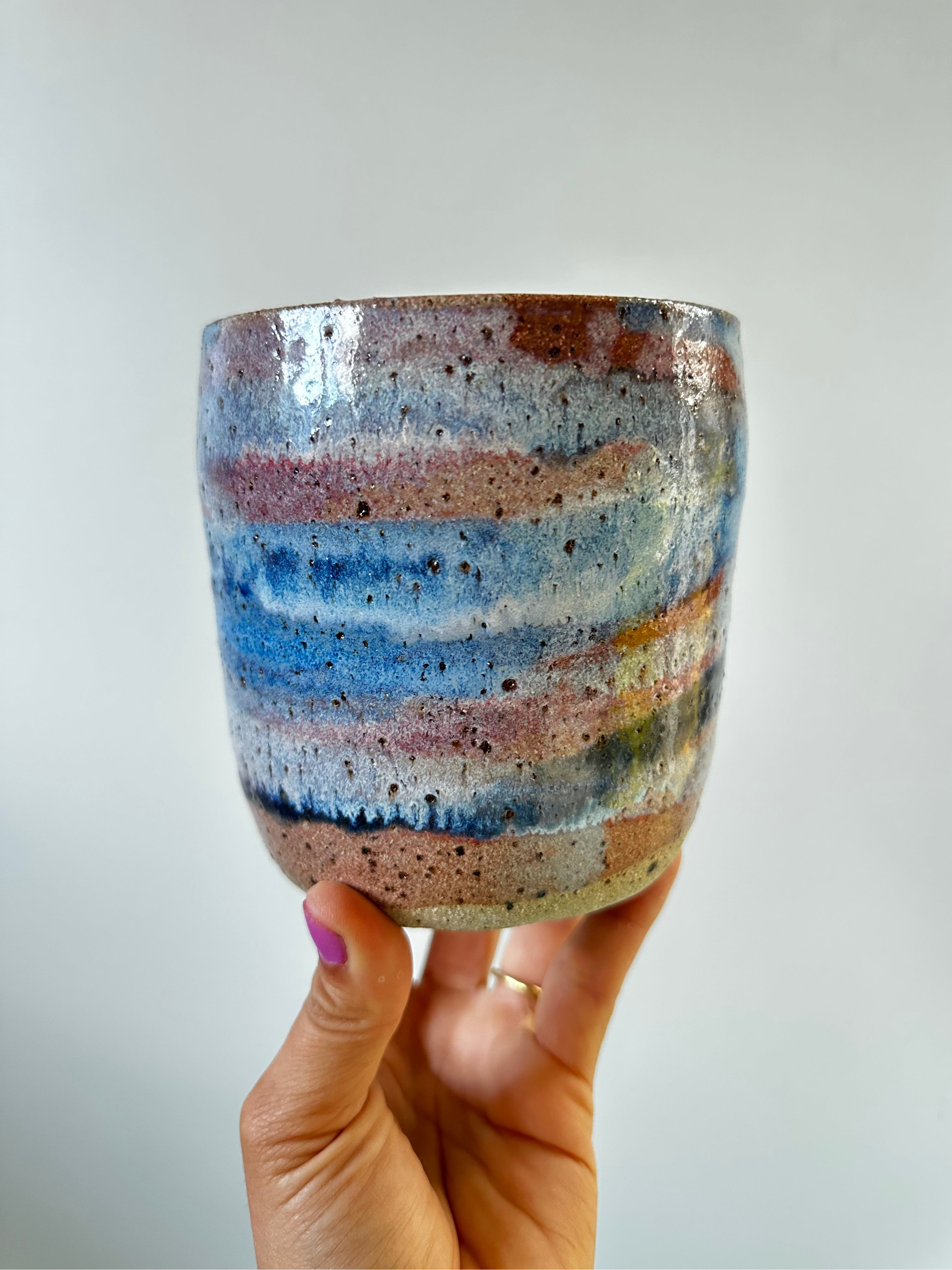 A hand holds up a medium planter with blue pink and purple sunset colours