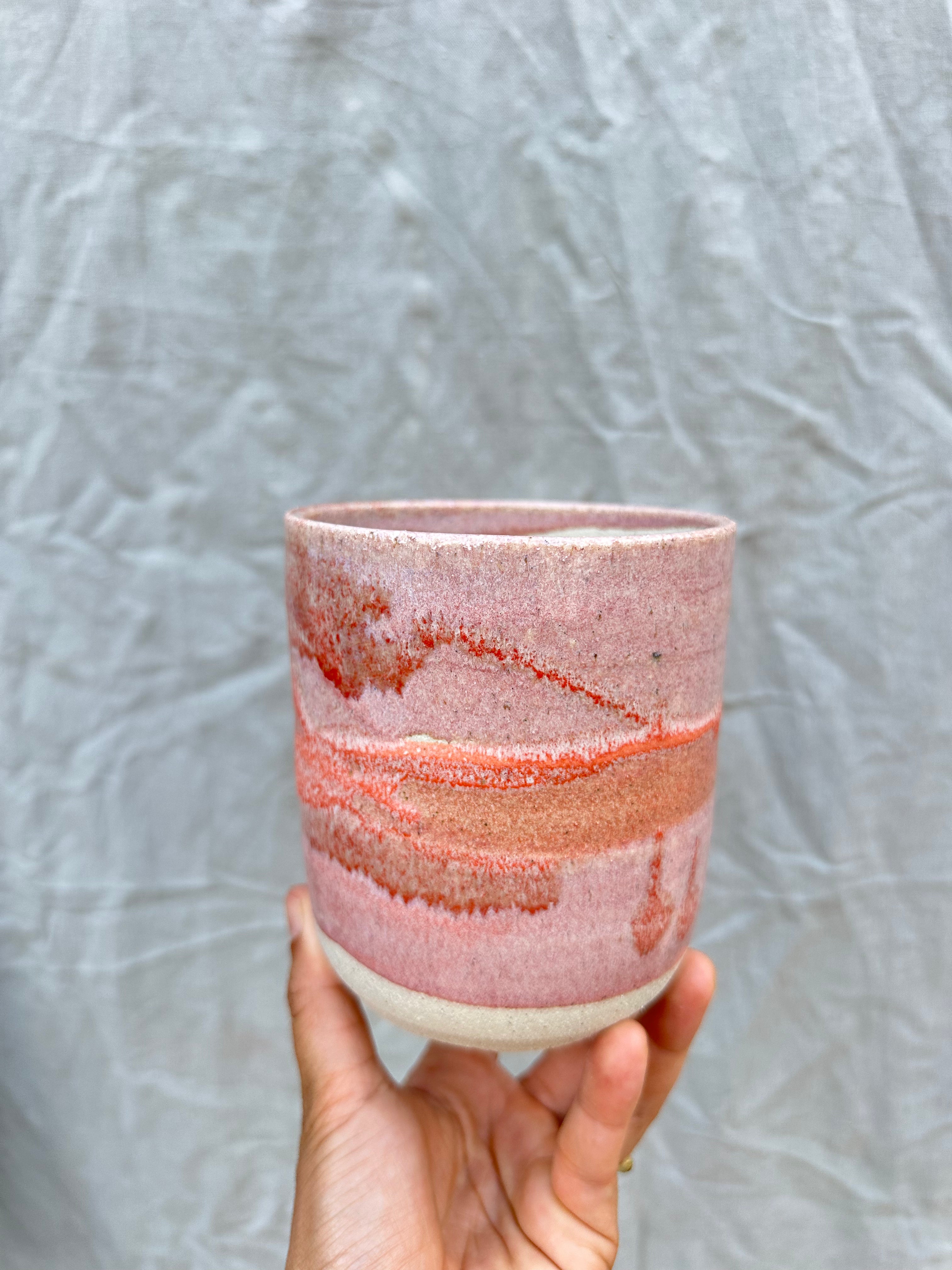 Hand holding a ceramic cup with a textured surface against a gray background