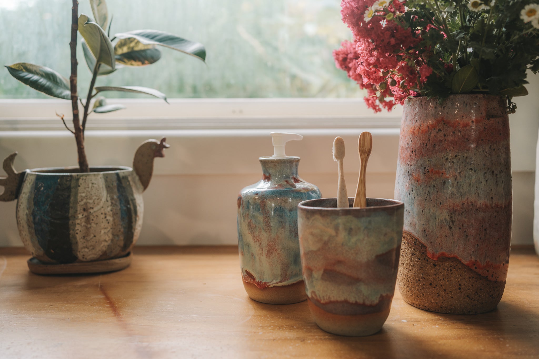 Set of ceramic jars and a vase with flowers on a wooden surface near a window.