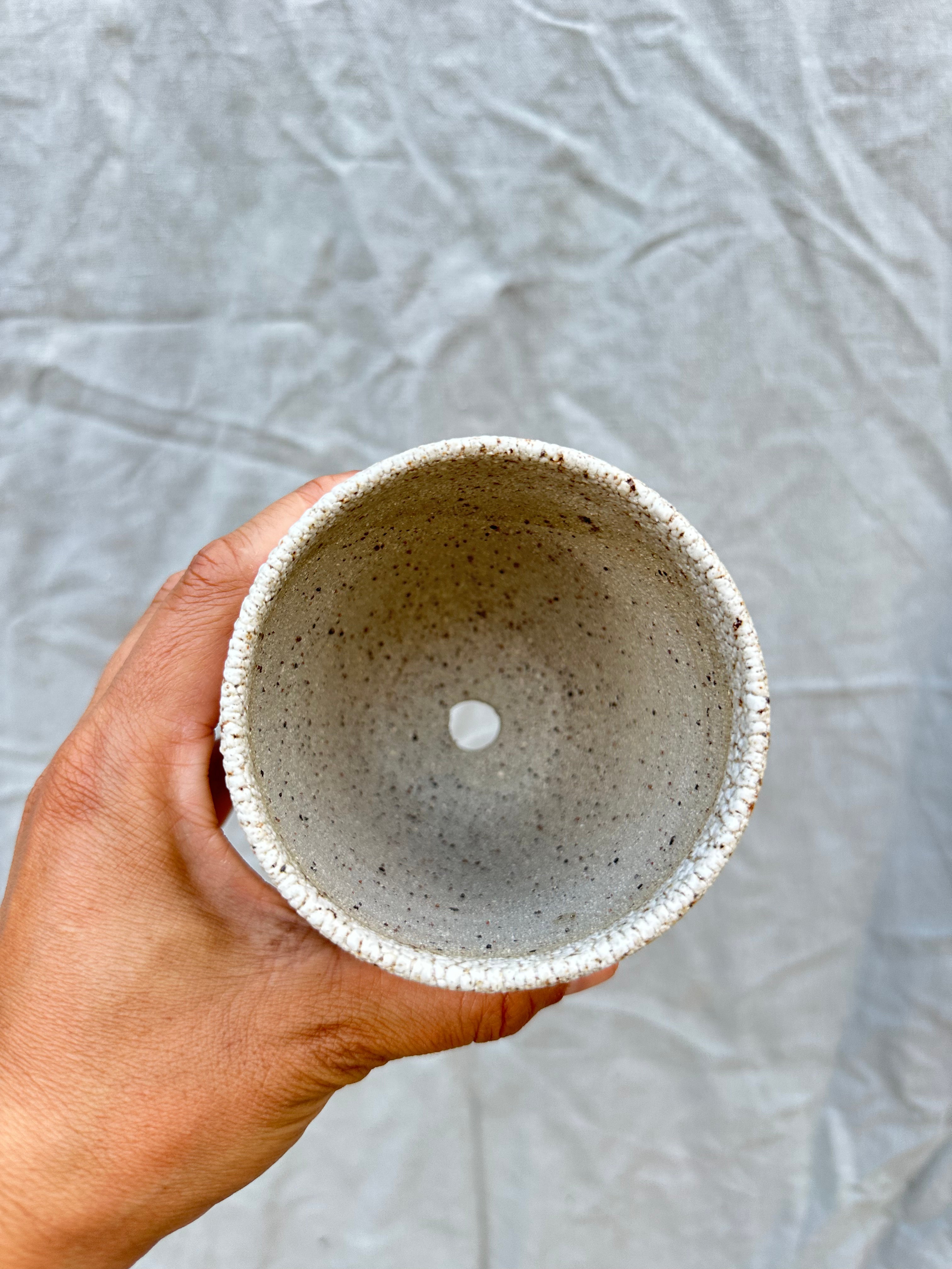 Hand holding a small speckled ceramic bowl against a textured gray background
