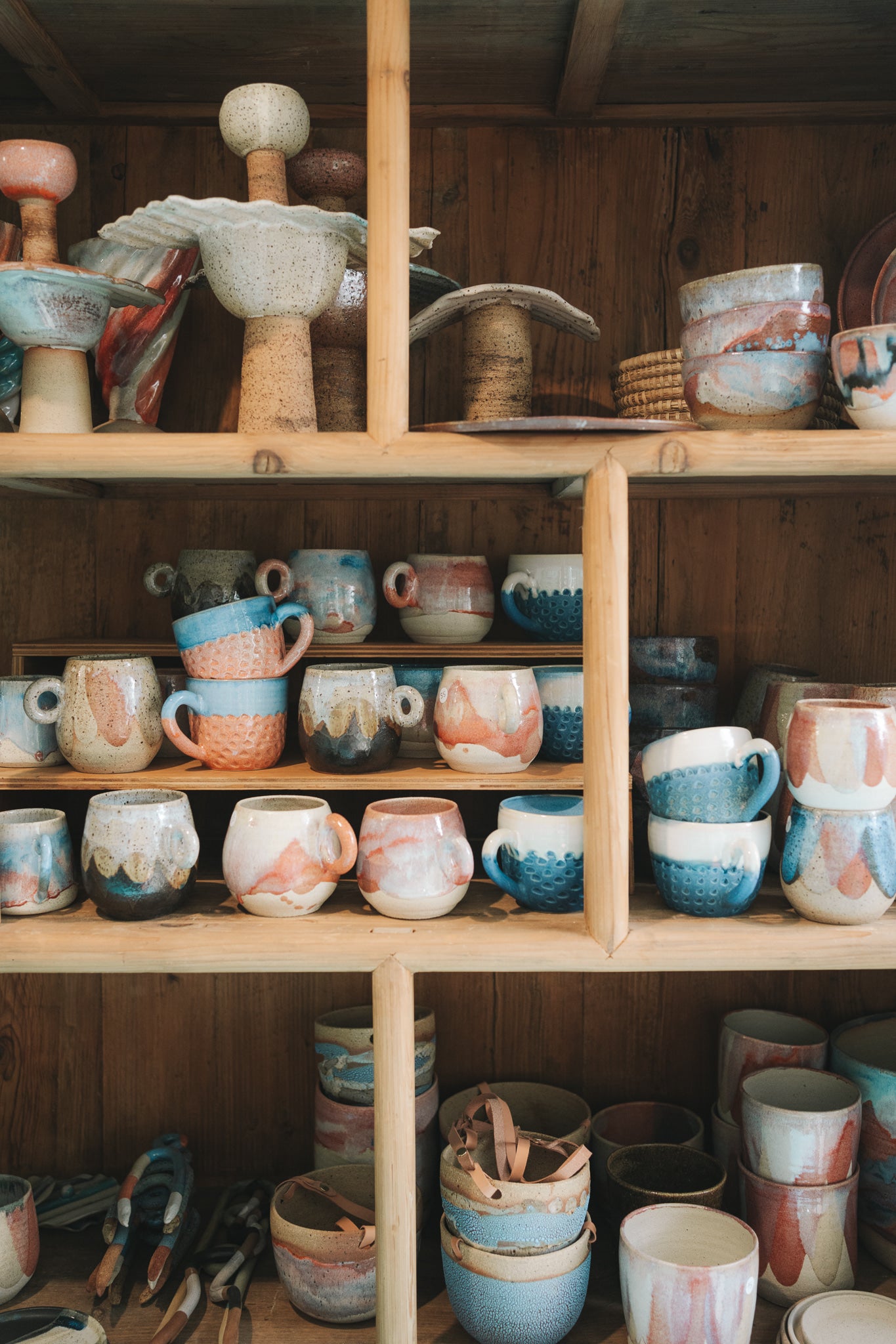 Wooden shelves filled with ceramic cups and bowls with a wooden wall background