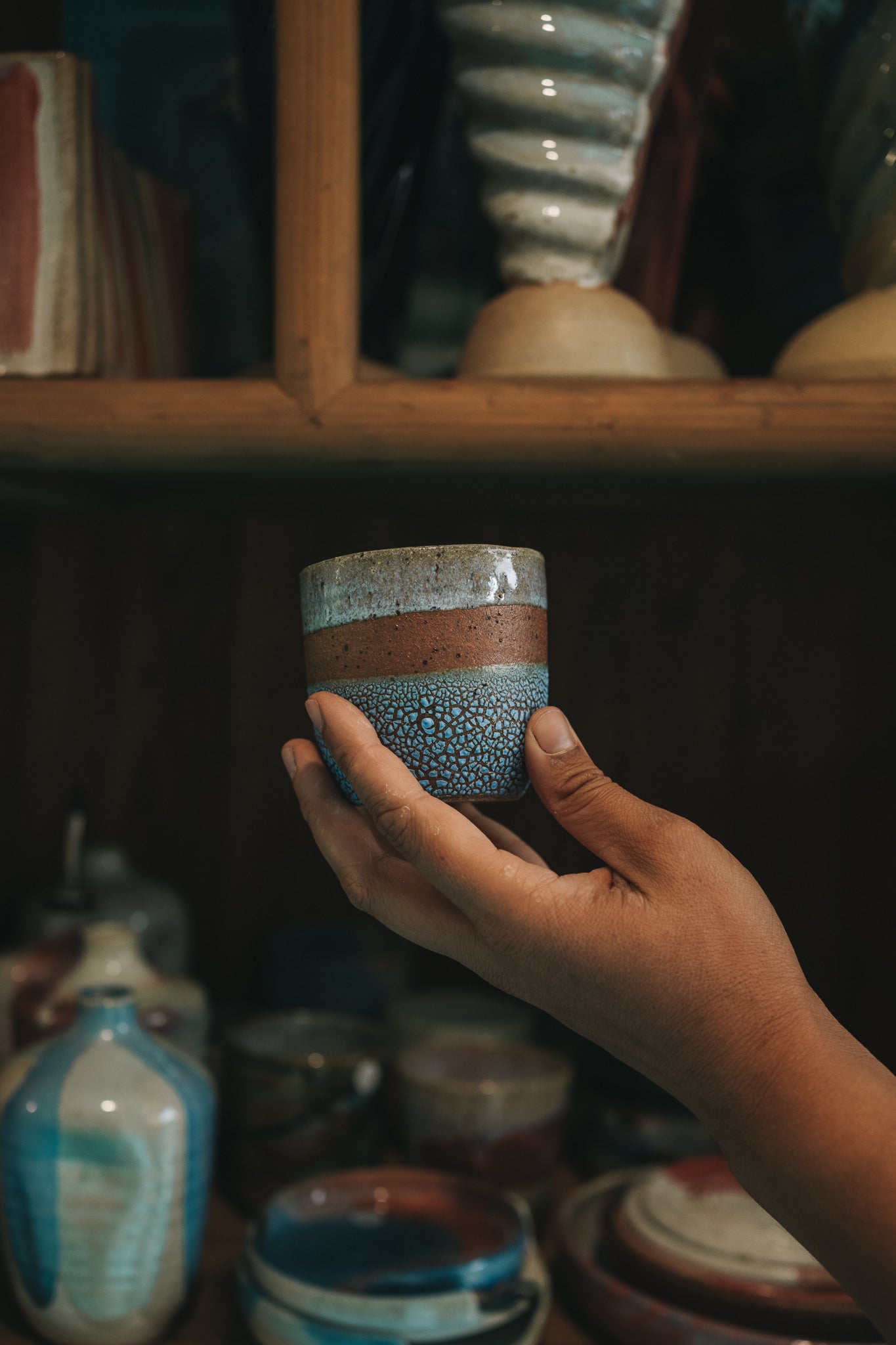 Hand holding a ceramic cup with a textured surface in a pottery studio.