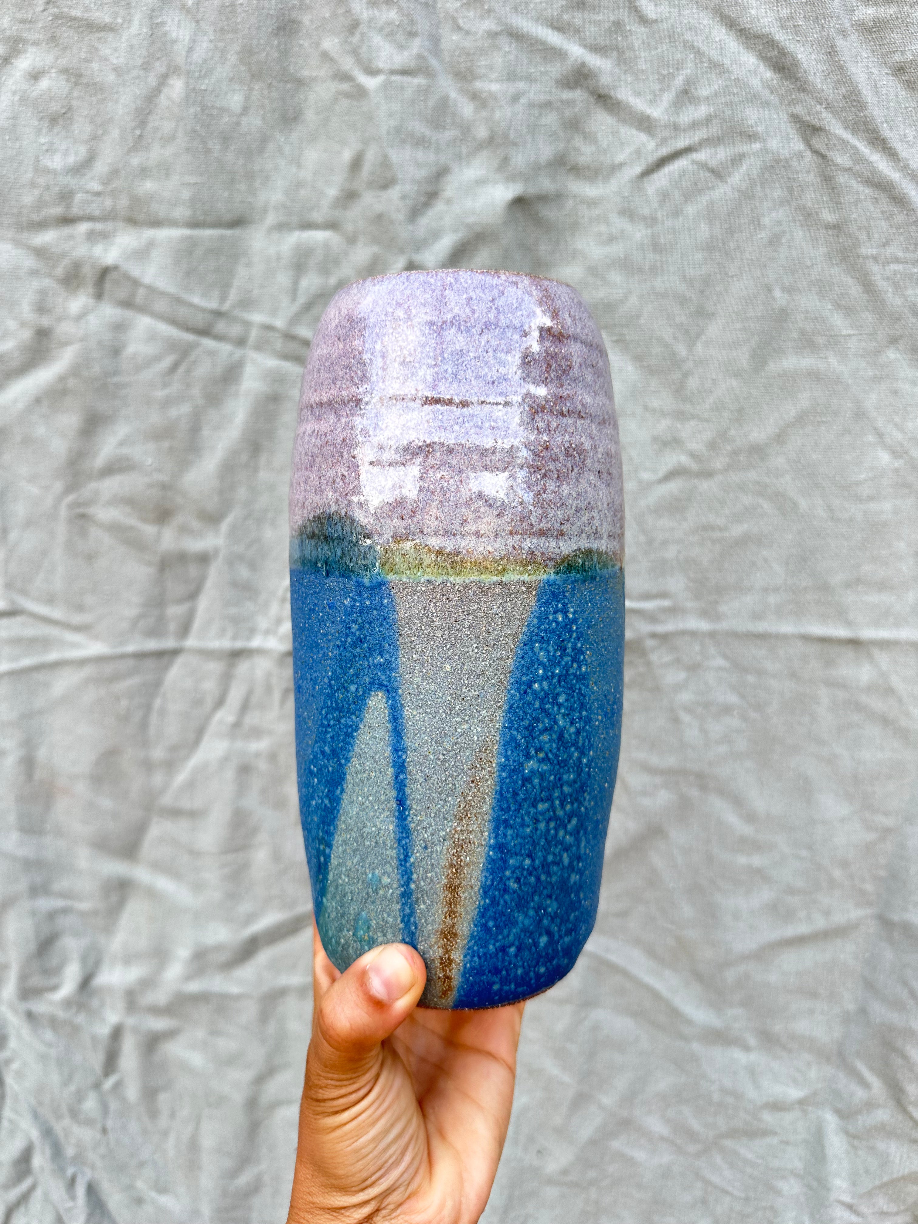 Cylindrical ceramic vase with gradient design held against a textured gray background